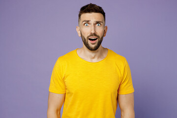 Young frightened fearful scared sad caucasian man wear yellow t-shirt looking camera with shocked facial expression isolated on plain pastel light purple background studio portrait. Lifestyle concept.