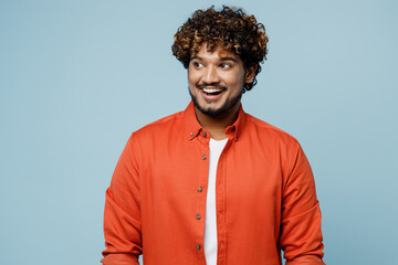 Fototapeta premium Young smiling happy fun cheerful Indian man wearing orange red shirt white t-shirt look aside on workspace area isolated on plain pastel light blue cyan background studio portrait. Lifestyle concept.