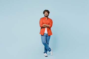 Full body smiling young Indian man wear orange red shirt white t-shirt hold hands crossed folded...