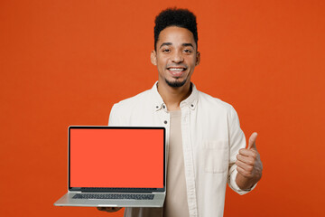 Young student IT man of African American ethnicity wear light shirt casual clothes hold use work on laptop pc computer with blank screen workspace area show thumb up isolated on orange red background.