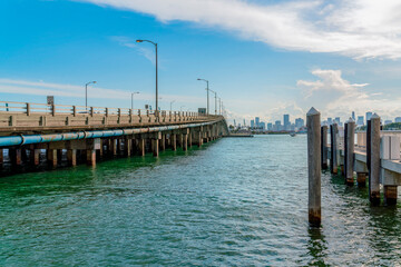Fototapeta premium Miami Beach Marina near the bridge over the Meloy Channel in Miami, Florida. There is a bridge with lamp posts heading to the city on the left and dock pillars on the right.