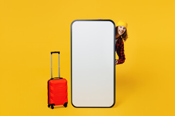 Traveler fun man wear casual clothes stand near big huge blank screen mobile cell phone bag suitcase isolated on plain yellow background studio. Tourist travel abroad in free spare time rest getaway.