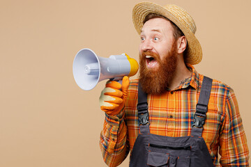 Young bearded man wear straw hat overalls work in garden hold megaphone scream announces discounts sale Hurry up isolated on plain pastel beige color background studio portrait. Plant caring concept.