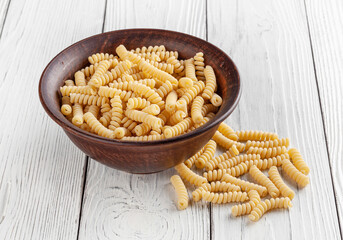 Uncooked fusilli pasta in ceramic bowl on white wooden background