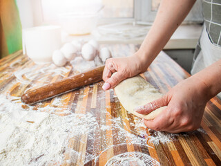 woman in apron rolls out dough with rolling pin, cooks at home, close up 