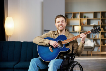 Handsome man with a disability sitting in wheelchair playing on guitar at home