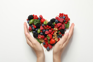 Female hands and heart made of berries on light background