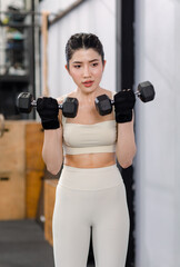 Fototapeta na wymiar Asian young female fit strong body sporty athletic fitness model in sport bra legging gloves standing posing holding lifting metal dumbbell weight training arms exercise at CrossFit gym.