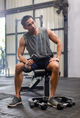 Obraz premium Asian young muscular fit strong body sporty athletic male fitness model in workout sleeveless sportswear holding lifting metal dumbbell weight training arms exercise at CrossFit gym