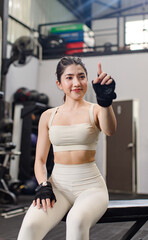 Asian young muscular fit strong body sporty athletic sexy female fitness model sitting smiling taking break after workout exercising weight training in gym.