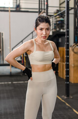 Asian young muscular fit strong body sporty athletic sexy female fitness model in sports bra leggings and gloves standing posing showing biceps muscle arm after workout exercising training in gym