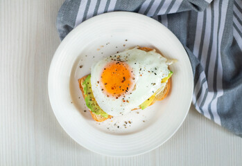 A kind of healthy toast with cream cheese, avocado and fried eggs on a dough on a plate close-up,flat lay