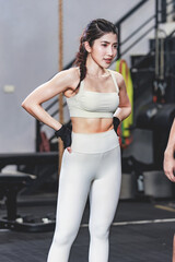 Asian young muscular fit strong body sporty athletic sexy female fitness model in sports bra leggings and gloves standing posing showing biceps muscle arm after workout exercising training in gym