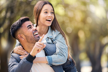Couple, outdoor and pointing at surprise for love, care and happiness together in summer. Young man and woman at nature park for piggyback, laughing or wow at space on happy date or vacation to relax