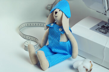 Close up cute, funny smiling sewed stuffed rabbit toy in blue design costume sitting near measure...