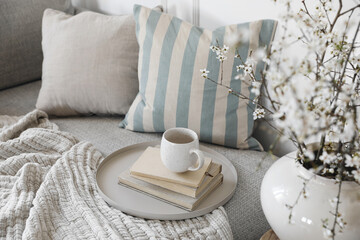 Spring interior still life. Cup of coffee, tea on pile of books. Round beige table. Blossoming...