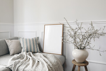 Naklejka na ściany i meble Modern spring scandinavian living room interior. Wooden picture frame, poster mockup. Sofa with linen pale blue striped cushions. Cherry plum blossoms in vase. Elegant stylish minimal home decor.