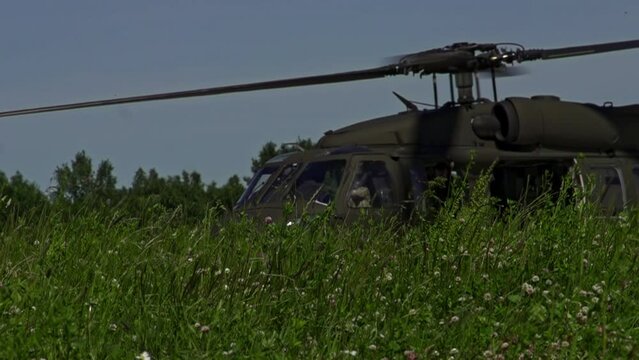 Slow motion rotors spinning on blackhawk military helicopter in grass