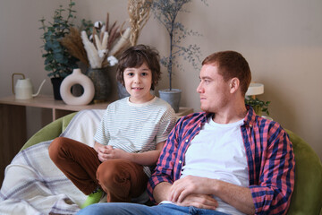 Cheerful father and son moment on a cozy couch, beaming at the camera. Navigating the Joys and...