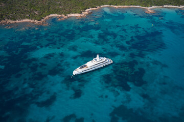 Large white yacht along the coastline at anchor. Large white modern mega yacht on transparent blue water, anchorage top view.
