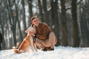 Sitting and embracing the dog. Man having a walk with his akita inu dog outdoors in the park at winter