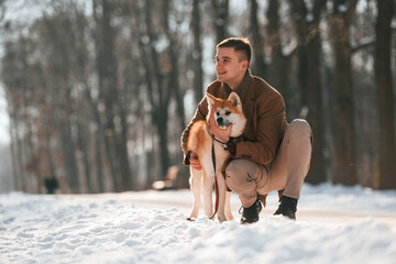 Sitting and embracing the dog. Man having a walk with his akita inu dog outdoors in the park at winter