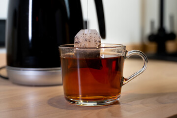A teapot pouring boiling water into a cup. A bag of black tea is put in a mug.