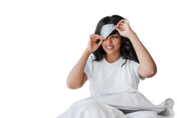 Young African American girl with wavy hair sitting on bed under blanket takes off sleeping mask looks away toothy smiles against transparent background, Cheerful young Brazilian woman, morning, hotel.