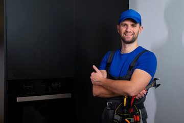 Portrait of a handyman in a blue uniform standing in the renovated kitchen of the house. 