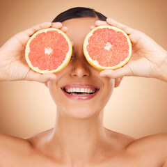 Beauty face, laugh or happy woman with grapefruit for fruit detox, healthcare or natural facial skincare routine. Vitamin c food product, fun studio or playful female nutritionist on brown background