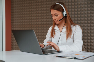 In headphones. Beautiful young woman is sitting by laptop in the office