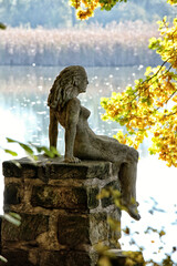 Statue of the girl sitting on the stone pole by the pond