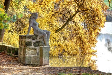 Concrete statue of girl nymph sitting on the bridge pole by the pond