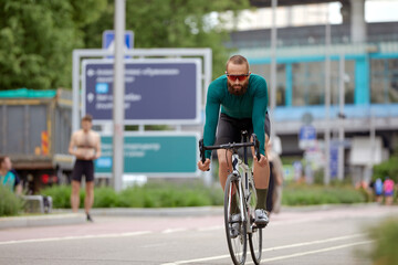 A cyclist man rides a bike in a city park along a bike path.