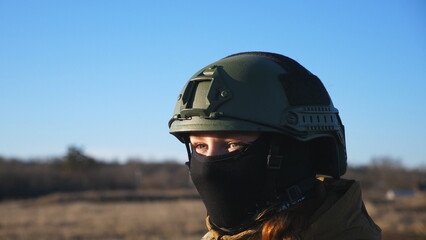 Dolly shot of ukrainian army woman in helmet and balaclava looking at sunset. Female military woman standing against background of blue sky. Victory against russian aggression. Concept of end of war