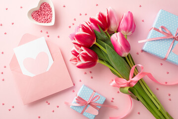 Mother's Day decorations concept. Top view photo of bouquet of tulips blue gift boxes with bows envelope postcard with heart and saucer with sprinkles on isolated pastel pink background