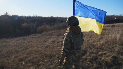 Dolly shot of female ukrainian army soldier holds a waving national banner on sunny day. Woman in...