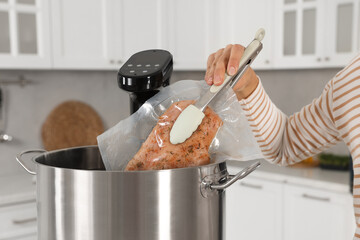 Woman putting vacuum packed meat into pot with sous vide cooker in kitchen, closeup. Thermal...