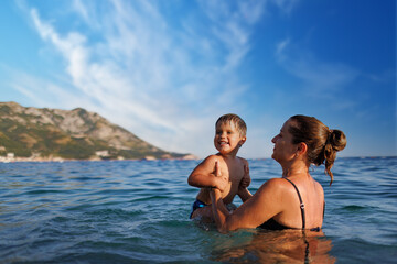 Fototapeta na wymiar Cheerful mother plays with her son in the sea