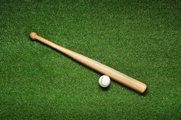 Fototapeta na wymiar Wooden baseball bat and ball on green grass, flat lay. Sports equipment