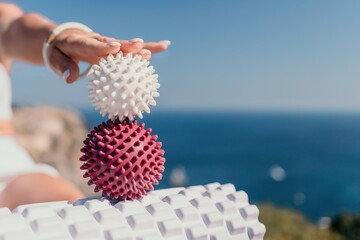 Woman sea pilates. Sporty happy middle aged woman practicing fitness on yoga mat with massage balls and roller near sea, smiling active female outside, enjoying healthy lifestyle, harmony