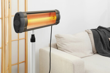 Functional electric infrared heater near sofa indoors