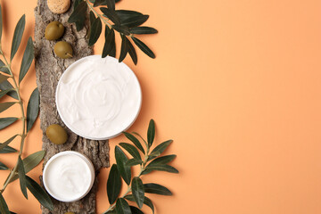 Fototapeta na wymiar Flat lay composition with jars of cream and olives on pale orange background. Space for text