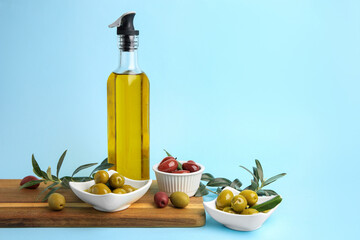 Bottle of oil, olives and tree twigs on light blue background, space for text