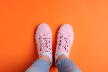 Woman in stylish sneakers standing on orange background, top view