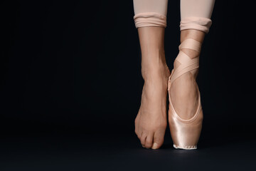Ballerina in pointe shoe dancing on black background, closeup. Space for text