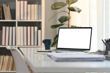 White working desk in modern home office with laptop computer, coffee cup and documents. Blank screen for advertising design