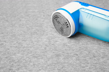 Modern fabric shaver on light grey cloth with lint, closeup. Space for text