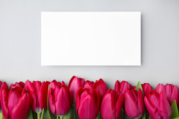 Many beautiful tulips and blank card on light grey background, flat lay