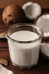 Glass of delicious vegan milk and coconut pieces on wooden table